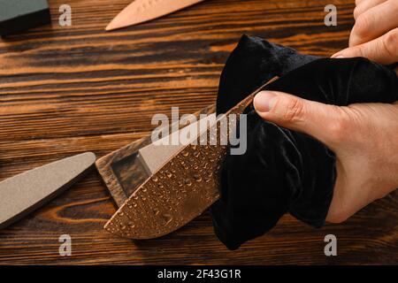 Uomo coltello di pulizia con straccio su fondo di legno, closeup Foto Stock