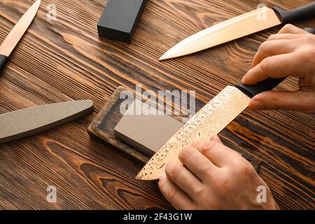 Uomo affilatura coltello su fondo di legno Foto Stock