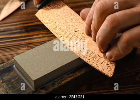 Uomo affilatura coltello su fondo di legno, primo piano Foto Stock