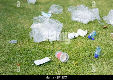 Bottiglie di plastica, rifiuti e una vecchia maschera viso giacente su erba in un campo Foto Stock
