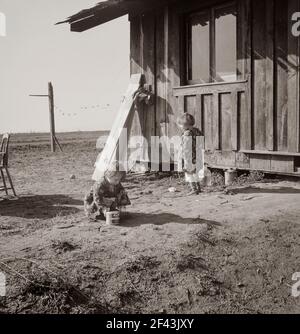 Sulle pianure ad ovest di Fresno, California. Famiglia di sette del ranch caseario dell'Oregon che hanno perso. "Abbiamo cercato di diventare troppo grandi, immagino. Le lattine di latte sono tutto che è lasciato del caseificio. Ora selezioni i bolls per fare cinquanta centesimi ad un dollaro un il giorno. Non possiamo lavorare tutti i giorni o forse potremmo arrivare.' Affitto per casa senza acqua o servizi igienici -sei dollari al mese. Piano accanto a raccogliere la frutta. "Dicono che se vieni in California, torni sempre, ma sono disposto a lasciarlo". Febbraio 1939. Fotografia di Dorothea Lange. Foto Stock