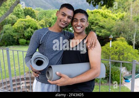 Ritratto di diverse coppie gay maschi che tengono tappetini yoga e. sorridente sul balcone Foto Stock