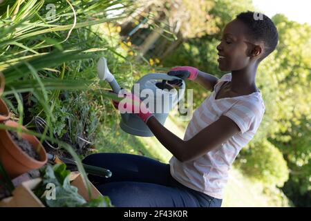 Donna afroamericana che fa giardinaggio e sorride sulla soleggiata terrazza giardino Foto Stock