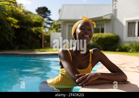 Ritratto di donna afroamericana in acqua appoggiata a bordo piscina sulla soleggiata terrazza giardino Foto Stock