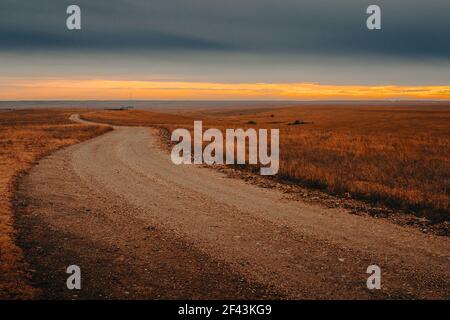 Vuota strada sterrata nella prateria che conduce al orizzonte durante il tramonto Foto Stock