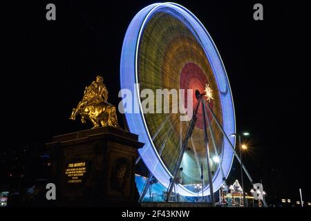 Golden Horseman agosto la statua forte di fronte a una ruota di ferro del mercato di natale. Foto a lunga esposizione di luci colorate della città. Foto Stock