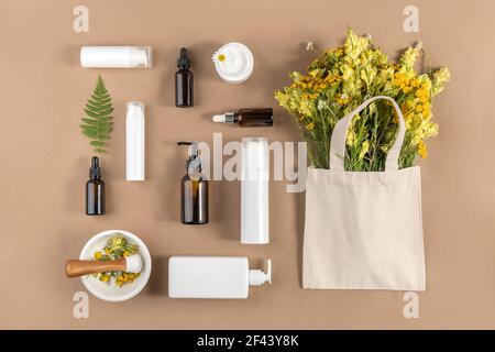 Bottiglie varie, provette, vasetto con cosmetici, fiori selvatici in sacchetto eco-tessile, mortaio con pestello su fondo beige. Concetto naturale di erbe organiche Foto Stock