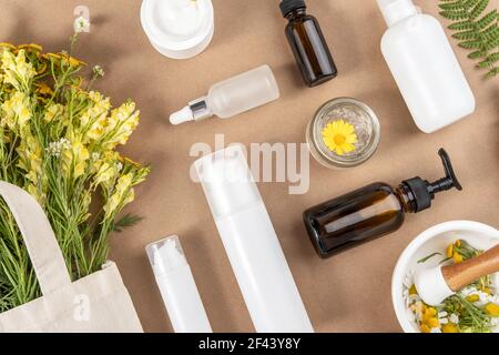 Bottiglie varie, provette, vasetto con cosmetici, fiori selvatici in sacchetto eco-tessile, mortaio con pestello su fondo beige. Concetto naturale di erbe organiche Foto Stock