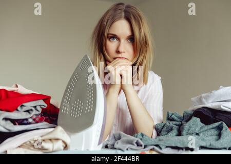 Triste giovane donna che stira abiti in soggiorno Foto Stock