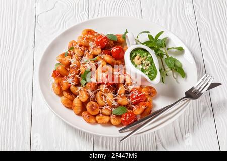 Gnocchi di patate piatto italiano con pomodori ciliegini e parmigiano su un piatto bianco con pesto di noci di anacardi menta, basilico e spinaci su un wo bianco Foto Stock