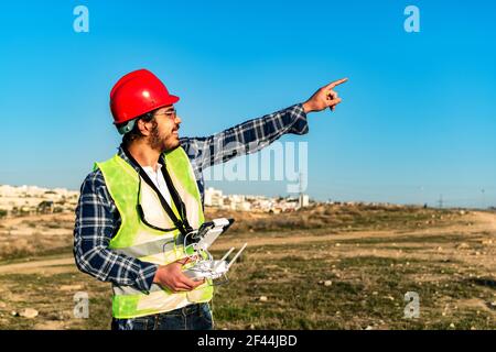 Un giovane lavoratore caucasico di costruzione che opera un drone su un cantiere Foto Stock