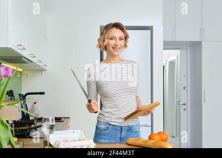 Una giovane donna positiva tiene in mano il coltello e il tagliere Foto Stock