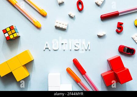 Giornata mondiale della consapevolezza dell'autismo. Piatto porre la parola bianca AUTISMO con cubi, puzzle, marcatori colorati e giocattoli sullo sfondo blu Foto Stock