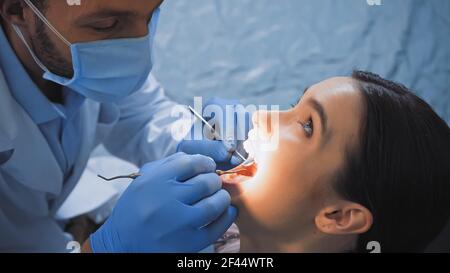 stomatologo in maschera medica che esamina i denti del paziente con dentista strumenti Foto Stock