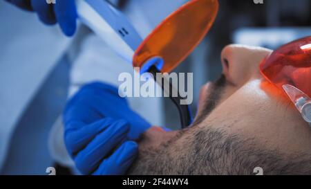 vista ritagliata del dentista che tiene la lampada ultravioletta vicino al paziente Foto Stock