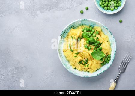 Purè di patate con burro, piselli verdi, cipolle, basilico in una ciotola bianca su un fondo di ardesia, pietra o calcestruzzo leggero. Vista dall'alto con primo piano. Foto Stock