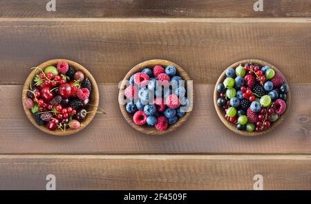 Vista dall'alto. Frutta e bacche in ciotole su sfondo di legno. Frutta mista con spazio di copia per il testo. Bacche miste su sfondo di legno. Vari freschi Foto Stock