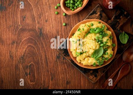 Purè di patate con burro, piselli verdi, cipolle, basilico su un rustico sfondo di legno. Vista dall'alto con primo piano. Foto Stock