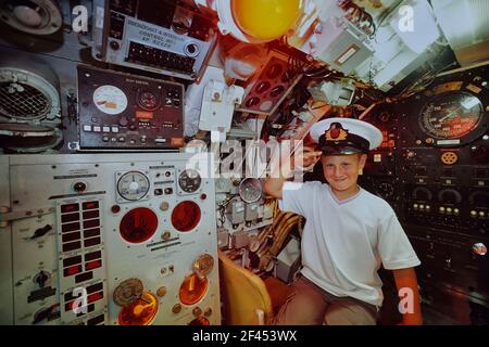 Ragazzo giovane che indossa un cappellino della Marina ufficiale che saluta dall'Helm della stazione del pilota a bordo del sottomarino di classe Oberon HMS Ocelot. Sottomarino HM Ocelot. Porto storico di Chatham. Kent. Inghilterra. REGNO UNITO Foto Stock