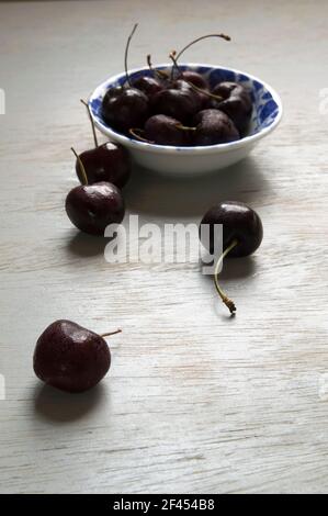 Ciliegie nere su una ciotola vintage bianca e blu su un tavolo di legno. Foto Stock