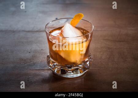 Cocktail vecchio stile con Whiskey su un tavolo in legno con torsione arancione in un elegante bicchiere in vetro di cristallo retro Foto Stock