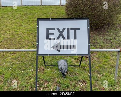 Free Standing Metal Exit Sign pesato da sacchi di sabbia da Una Grass Bank con indicazioni per i veicoli che lasciano un'area esterna Parcheggio auto nella città di Exeter Foto Stock