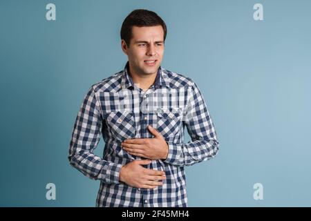 Giovane uomo sconvolto che soffre di crampi allo stomaco isolati su blu sfondo Foto Stock