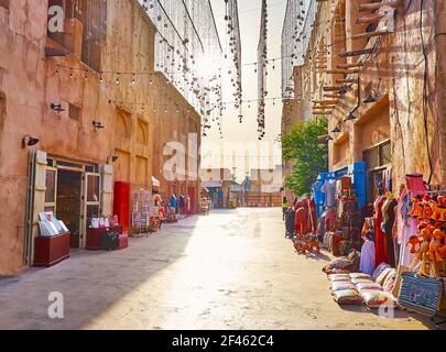 La passeggiata di mezzogiorno nella città vecchia con una vista su bancarelle turistiche, ghirlande sopra il vicolo e le vecchie case di argilla, al Fahidi, Dubai, Emirati Arabi Uniti Foto Stock