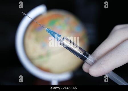 Vaccinazioni nel mondo, mano del medico con siringa sullo sfondo del globo. Concetto di assistenza sanitaria durante la pandemia di covid-19 Foto Stock