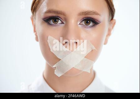 Colpo di testa di donna con la bocca tappata in primo piano isolato su bianco sfondo studio Foto Stock
