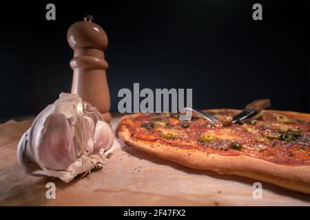 Freshky cotta, pizza casereccia Napoli posato su carta da forno subito dopo essere uscito dal forno. Aglio e salino in legno. Olive, acciughe, pomodori Foto Stock