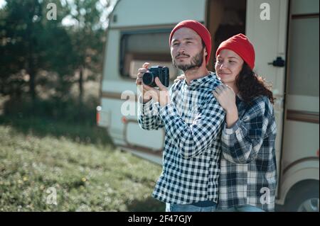 Accoppia in un plaid a scacchi arrostendo marshmallows sul fuoco vicino alla casa del rimorchio. Foto Stock