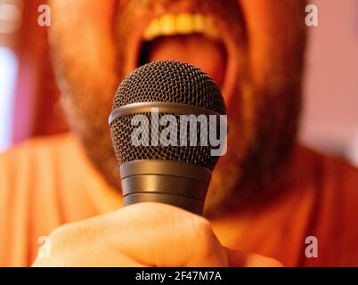 Un primo piano di un uomo che canta mentre tiene un microfono Foto Stock