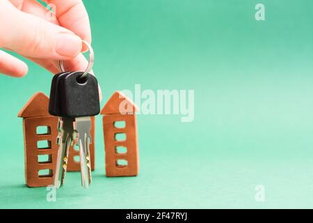 Mano femminile con due chiavi e case in mattoni in miniatura su sfondo verde Foto Stock