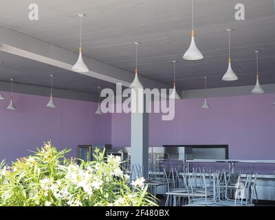 Sala da pranzo vuota con sedie rovesciate sui tavoli, fiori in primo piano e sfumature bianche sul soffitto Foto Stock