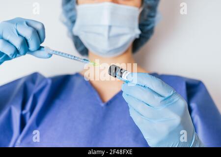 Le mani guanto chirurgiche di un medico che ritira il vaccino del coronavirus con una siringa. Foto Stock
