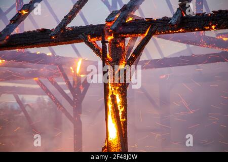 Bruciato fienile di legno con fuoco e scintille ancora brillare. Capriate e pali in legno. Foto Stock