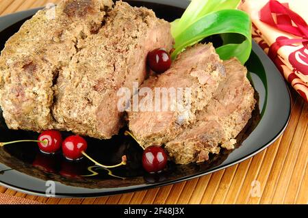 Succulenti fette di carne arrosto di manzo con ciliegia su un piatto nero. Carne al forno. Foto Stock