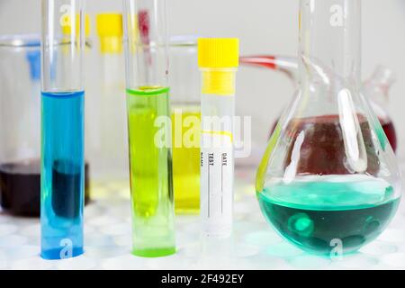 Uno shot isolato di una provetta vuota per il test del sangue e. alcune fiasche di vetro con liquidi colorati Foto Stock