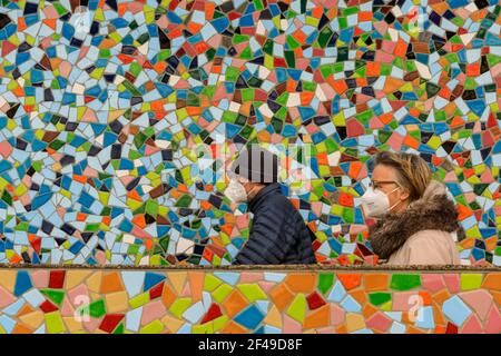 Dusseldorf, NRW, Germania, 19 marzo 2021. Due persone in maschere facciali FFP2/KN95 camminano oltre la parete a mosaico 'Rivertime' di Hermann-Josef Kuhna sulle rive del fiume Reno a Dusseldorf, capitale della NRW. È probabile che le misure di blocco aumenteranno ancora una volta in Germania, dal momento che il tasso di incidenza di 7 giorni salirà verso il punto cruciale di interdizione di 100 abitanti/100.000. Mentre oggi Dusseldorf ha un prezzo relativamente buono a 63, la Germania ha complessivamente visto aumentare i numeri a 95.6 Foto Stock