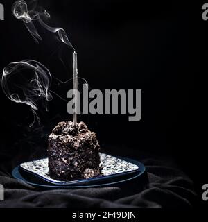 Torta al cioccolato fondente con una candela grigia soffusa su un piatto di porcellana, isolato, primo piano Foto Stock