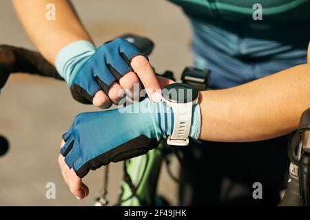 Primo piano di mani di ciclista femminile professionista in abbigliamento da ciclismo con smartwatch, controllando i risultati dopo aver fatto un allenamento, a cavallo in bicicletta Foto Stock