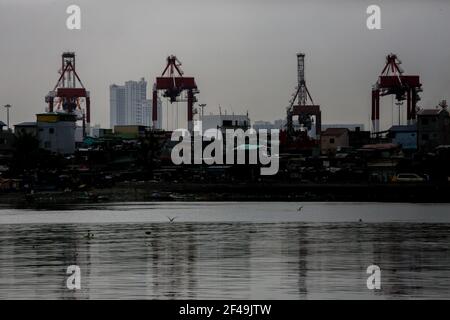 Le case sono viste accanto ad un porto marittimo a Manila come la capitale filippina segna un anno sotto una quarantena comunitaria per aiutare a combattere la diffusione del coronavirus. Filippine. Foto Stock