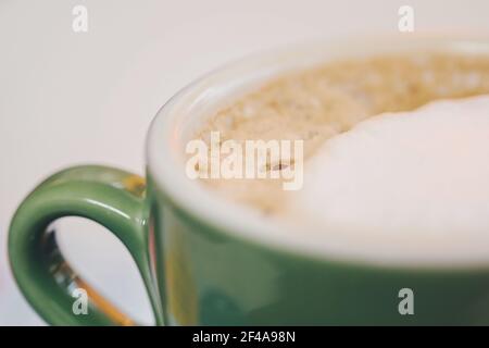 Caffè in tazza verde di cappuccino in ceramica con schiuma di crema, chiusura di tazza di cappuccino latte. Latte di caffè caldo in tazza di porcellana color giada. Messa a fuoco selettiva Foto Stock