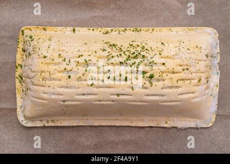 Pasta sfoglia surgelata con salmone adagiato su carta da forno, isolata su uno sfondo marrone vista dall'alto. Foto Stock