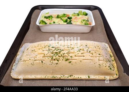 Pasta sfoglia surgelata con salmone e filetto di pollock con broccoli e mandorle tostate in salsa panna adagiata su carta da forno, isolata su un dorso bianco Foto Stock