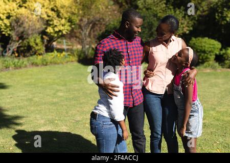 Sorridendo genitori afroamericani con figlia e figlio in piedi abbracciando all'aperto Foto Stock