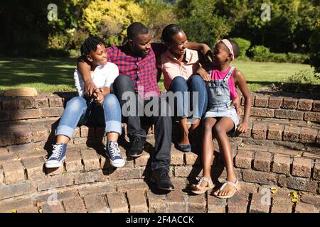 Sorridendo genitori afroamericani con figlia e figlio seduti abbracciando all'aperto Foto Stock