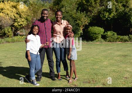 Sorridendo genitori afroamericani con figlia e figlio in piedi abbracciando all'aperto Foto Stock