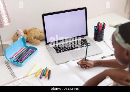 Vista sulle spalle della ragazza afroamericana seduto alla scrivania con il computer portatile che lavora a scuola Foto Stock